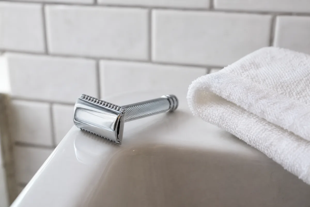 Rasoir de sûreté en métal posé sur le rebord d’un lavabo blanc